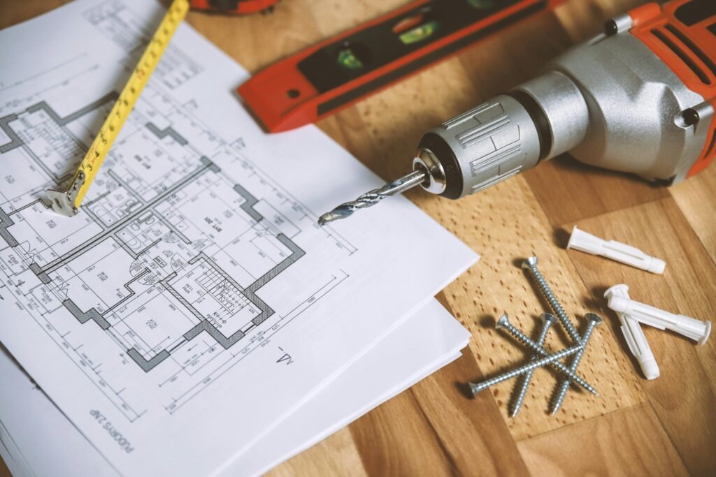 pexels-photo-834892-834892 Close-up of construction blueprint with tools like drill and screws on a wooden table.